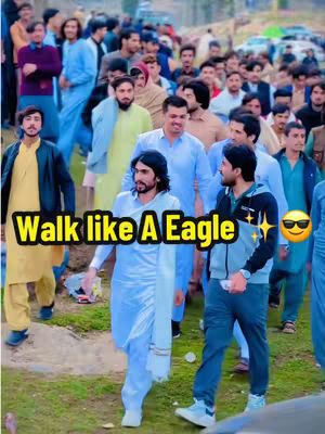 A crowd of people gathered outdoors, with several individuals in the foreground. The focus is on a group of men walking, with text overlays superimposed on the image.