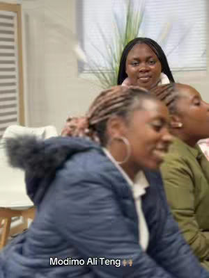 The cover image features three African women. The woman closest to the camera is wearing a dark blue jacket with a fur-lined hood. The two women behind her appear to be in an office setting. The text "Modimo Ali Teng" is at the bottom. The overall composition is straightforward, with a focus on the group interaction in a casual setting.