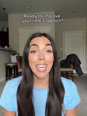 A woman with long dark hair and a blue shirt smiles at the camera. Text overlay reads, 'Ready to improve your little's speech?' The background features a domestic interior, with furniture. The lighting is bright, and the overall tone appears friendly.