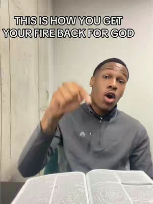 A young Black man with short hair and a gray shirt is featured, pointing downwards with his right index finger while speaking, He is seated at a table with an open book in front of him, potentially a Bible, and the background suggests a simple indoor setting.