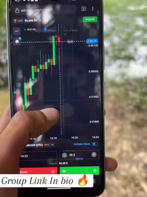 A close-up shot of a smartphone displaying a trading platform interface. The screen shows real-time stock charts with green and red candlestick patterns, and trading statistics. A hand is visible, interacting with the screen. The background is blurred.