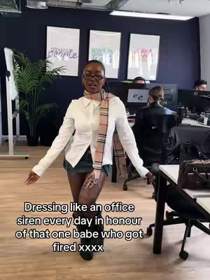 A woman in an office setting strikes a pose. She wears a white shirt, a scarf, glasses, and short denim shorts. Text overlays at the bottom of the image.