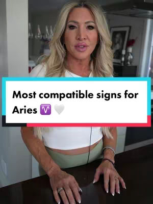 A woman stands in front of a kitchen wearing a white top and green leggings. A text overlay reads "Most compatible signs for Aries" in a teal and white box, with an Aries symbol and a heart emoji. The background includes a kitchen counter, a framed picture, and some glassware.