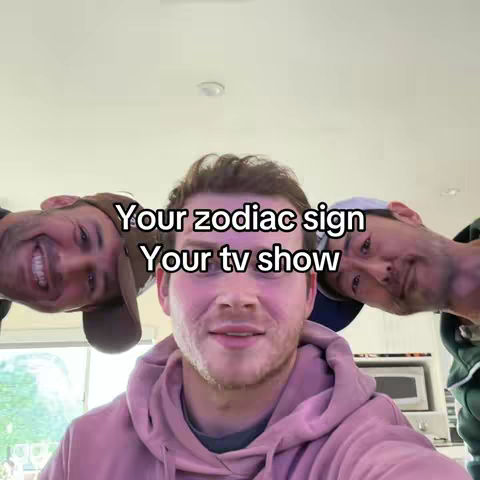 The cover image features three Caucasian men in a selfie-style shot, angled from their upper bodies. The man in the center is the primary focus, wearing a light pink hoodie and smiling. He is flanked by the other two men, positioned on either side, with one wearing a baseball cap. Text overlayed on the image reads, 'Your zodiac sign/Your tv show' in a casual font. The background appears to be a domestic setting.