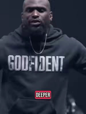 A man wearing a black hoodie with the word 'GODFIDENT' in large white letters is centered in the frame. The lower-left has a red banner with the text 'DEEPER'. The background is a dark, blurred setting.