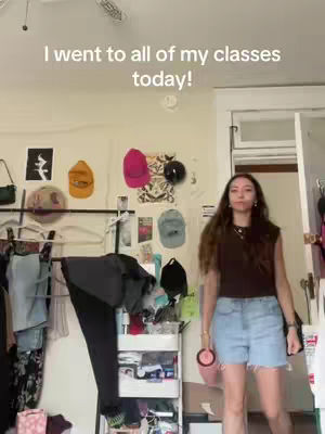 A person standing in a brightly lit room with various items hanging on the wall. The person is wearing casual clothes. The text overlay reads: I went to all of my classes today!