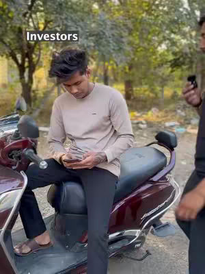 A young man sits on a maroon scooter, holding a phone and some cash. The background suggests an outdoor setting with trees.