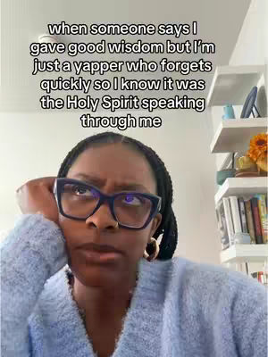 A woman with dark skin and black braided hair, wearing eyeglasses and a blue sweater, gazes towards the upper right with a thoughtful expression. Text overlays her head.