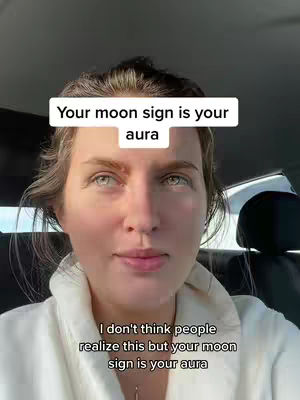 A selfie-style shot of a woman in a car, looking directly at the camera with a neutral expression. Two overlaid text boxes are present on the image. The woman is wearing a white top and a light-colored robe over it. The background is a blurred view of a car interior.
