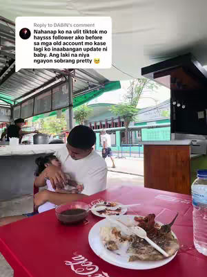 A man is holding a young child, both are seated at a table with food, in an outdoor setting. A comment overlay is positioned above them, and the overall environment suggests a casual restaurant or eatery.
