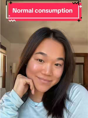 A woman with long dark hair is smiling and looking at the camera. She has fair skin and is wearing a light blue shirt which is a basic button down. The background has a window letting in muted light and a glimpse of a hallway. A text box at the top says “Normal consumption”.