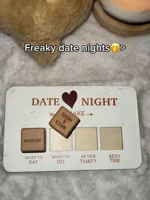 The cover image shows a close-up of a white Date Night card with four blank squares. The card has the words "DATE NIGHT" in a dark brown font. A brown heart is in the center. There are two wooden blocks with words on them. There is a blurred plush material in the background and a candle.