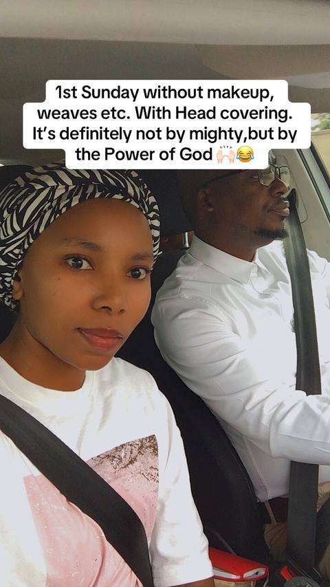 A woman and a man are seated inside a vehicle, presumably driving. The woman is in the foreground, looking towards the camera. She is wearing a white shirt and a head covering with a black and white patterned design. The man, who is wearing a white shirt and glasses, is in the background on the right, appearing to be driving. There is text overlaid on the image in a white rectangle, and the color of the image leans towards a natural, slightly desaturated tone.