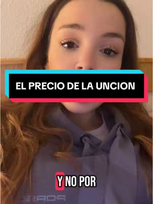 A young woman with long brown hair is centered in the frame. She is wearing a blue hoodie with a tie detail. Overlaid on her image are two rectangular text boxes: the top one in black that reads 'EL PRECIO DE LA UNCION', and the lower one in red with text 'Y NO POR'. The text boxes are positioned to be easily readable without obscuring her face. The background is a plain, warm-toned surface. 