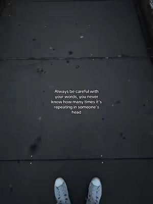 The image shows a top-down perspective of a dark surface, possibly concrete or asphalt, with a quote overlaid in white text. Two pairs of feet in sneakers are visible at the bottom of the image. The quote is placed centrally, above the feet. The overall aesthetic is somber, with the dark background and text suggesting a reflective topic. The composition is simple, drawing focus to the text and the implied subject's point of view.