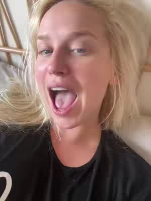 A selfie with a person laying down in bed with blonde hair and an open mouth.
