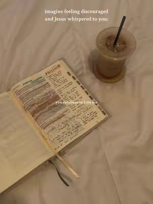 The image shows an open notebook with handwritten notes and highlights, a drink in a clear glass with a straw, all resting on a slightly wrinkled, light-colored surface resembling a bed or sheet. The overall aesthetic is soft and warm-toned.
