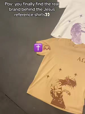 The cover image features a top-down view showcasing several t-shirts. The shirt on the bottom is a tan color, possibly a Gildan shirt, featuring two graphic images on the front: a muscular figure with a crown of thorns and what appears to be the letters 'A'and 'Ω'. The white colored shirt on top includes a graphic of a face beside a star.