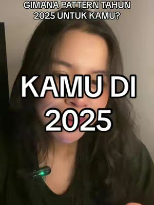 A young woman with dark hair is centered in a vertical video frame. She's looking towards the viewer, with text overlays. Above her head 'GIMANA PATTERN TAHUN 2025 UNTUK KAMU?' is written in white. Large white text 'KAMU DI 2025' is underneath. The lighting appears to be soft, and the background is out of focus.