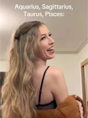 A woman with long blonde hair smiles, looking over her shoulder. The background is blurred, with hints of a room and a light fixture.