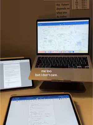 A workspace setup featuring a laptop, two tablets, and stationery items on a desk. The lighting leans warm, and the composition is an overhead shot focused on productivity or study.