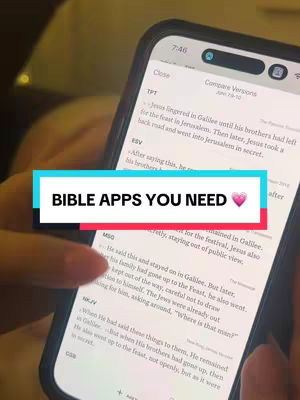 A person's hand holds a smartphone, displaying a bible app interface. The phone screen shows text from different bible versions. A colorful banner overlays the screen, displaying "BIBLE APPS YOU NEED" with a heart emoji.