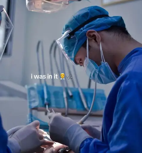 A medical professional, seen from the side, is performing a procedure, with tools and the patient's view visible.