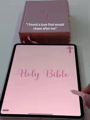 The image shows a pink Bible and a tablet displaying the words 'Holy Bible' in pink with a stylus touching the screen. Above, a pink Bible is closed. The overall composition is soft and centered, with a focus on religious themes.