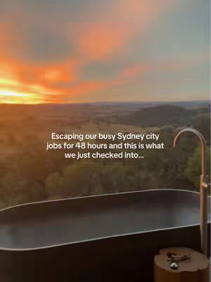 The cover image showcases a serene outdoor scene during sunset. A dark bathtub is in the foreground with a silver faucet, and what looks like a stone side-table with some keys on it. The background is a breathtaking view of green rolling hills under a vibrant sky of oranges, pinks, and blue. The overall composition suggests relaxation and luxury, capturing a moment of escape in a scenic setting.