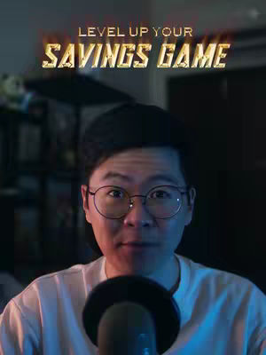 A man with glasses is in the middle of the frame, with the text "LEVEL UP YOUR SAVINGS GAME" across the top. He is wearing a white t-shirt and a microphone is in front of him.