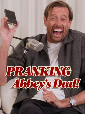 A man laughing with his mouth wide open while holding a smartphone. He has a microphone in front of him and the words 'PRANKING Abbey's Dad!' are overlaid on the image.