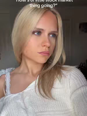 A close-up shot of a woman with blonde hair, appearing thoughtful. The top half of her torso is visible, wearing a white, textured sweater. The background is soft and out of focus.