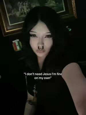 A selfie-style shot featuring a person with dark hair and prominent facial piercings, centered in the frame. The background is dimly lit, featuring blurred elements of framed pictures and decor. The person has a neutral expression. The overlaid text gives an impression of defiance.