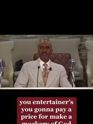 A man in a light colored suit stands in front of a microphone with a focused expression. The background is a blurred space with what appears to be chairs. At the bottom of the image, a red text overlay states a critical religious message.