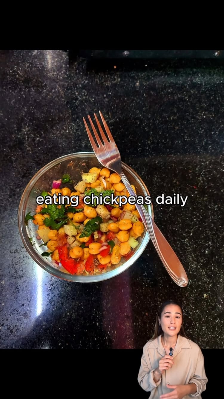 A woman is speaking, holding a microphone. The background features a glass bowl of food with a fork. Text overlay says "eating chickpeas daily".