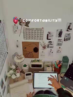 The image shows a study desk scene with a lot of items placed on top, a hand is pointing at the tablet screen with documents and a laptop on the right. Above the desk are decorations and a calendar. The overall composition is bright.