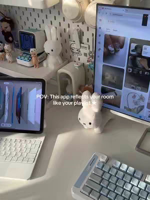 A well-lit room with a white desk, featuring an iPad with a keyboard, a computer monitor displaying an app interface, and decorative items like a white bunny figure and a small clock. The composition uses a POV perspective.