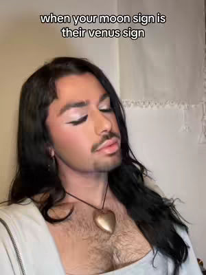 A person with long black hair, full makeup, and a necklace in a close up shot.