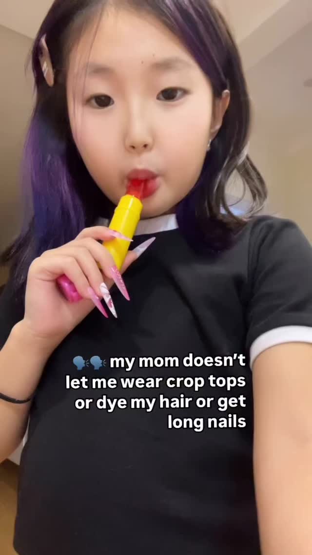 A young woman with long, colorful nails and partially purple hair holds a red and yellow popsicle near her mouth, looking directly at the camera. The background is a plain wall. Text overlays the image.