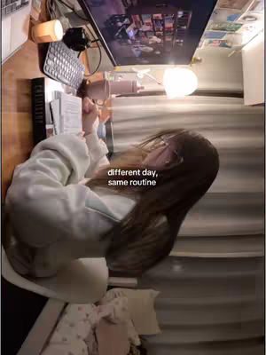 The cover image shows a person with long hair, resting their head on their hands, at a desk with a laptop and other items. A text overlay reads, 'different day, same routine' The image has a warm light and appears to be set in the creator's room.