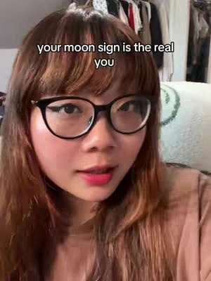 A woman with brown hair and glasses is the primary subject, facing towards the camera. The background is somewhat blurred, showing clothes and possibly a pillow. The overall composition is a close-up shot focusing primarily on the woman's face and upper body.