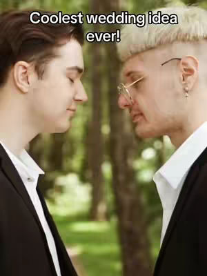 Two men face each other with their foreheads touching. They are wearing suits and white shirts. The background is blurred, suggesting an outdoor setting.