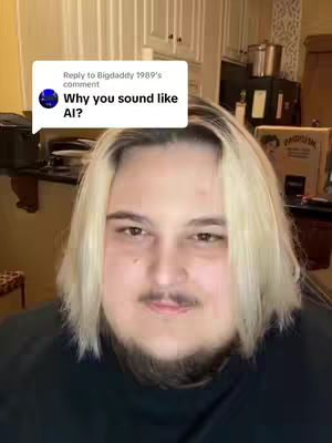 A person with light blonde hair, a goatee, and heavy stubble is the central focus. A speech bubble overlay contains the text “Why you sound like AI?”. The background features a kitchen interior with cabinets and appliances.