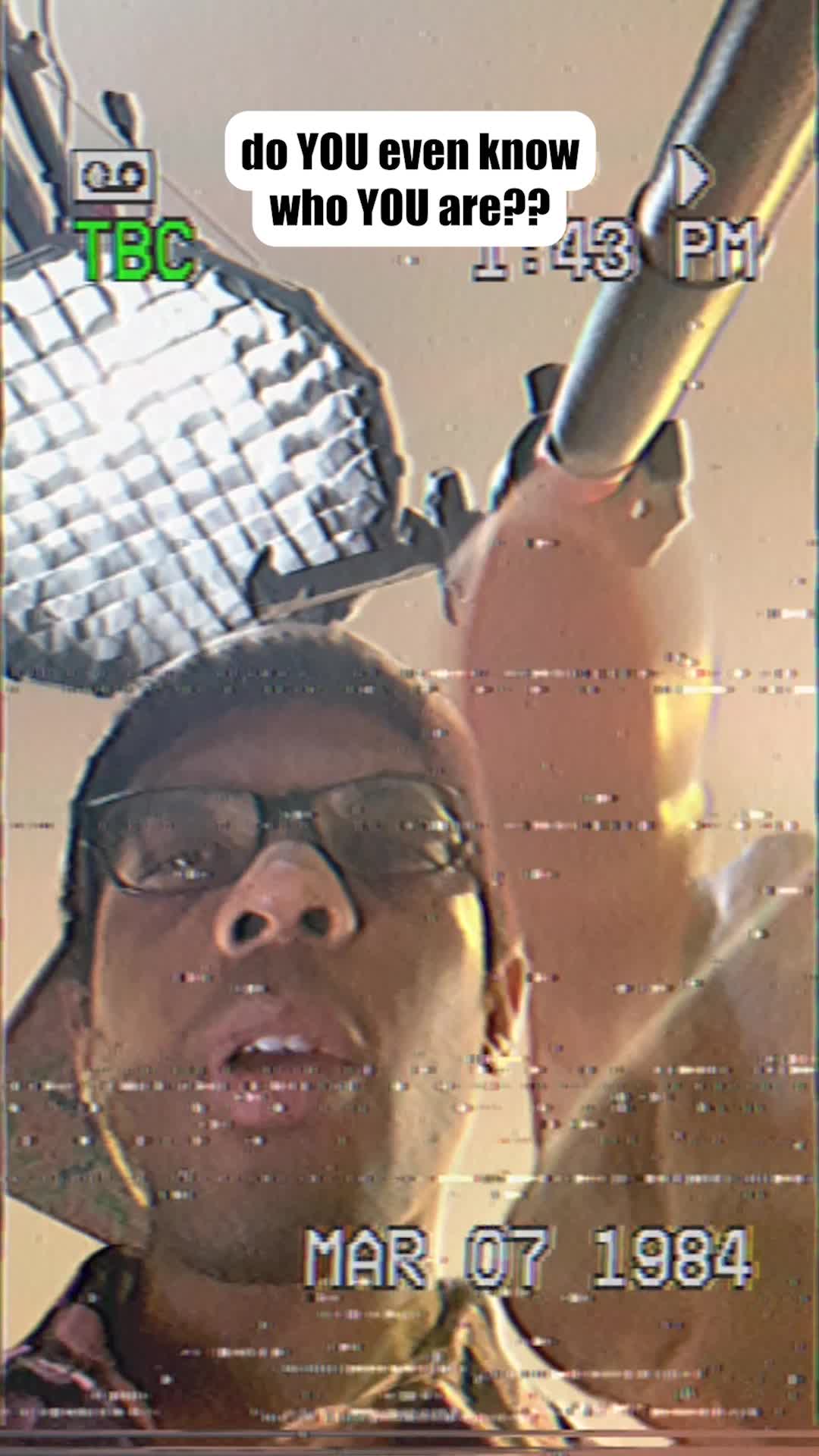 The cover image shows a medium close-up shot featuring a person in glasses and a cap, facing the camera with an open mouth. The person is framed against a background with bright light sources and overlaid with a glitch effect and a retro date stamp. The hook text reads "do YOU even know who YOU are??".