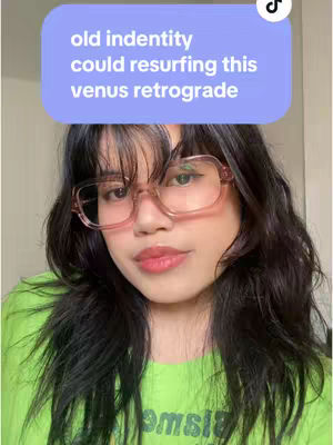 A selfie-style image featuring a young woman with long, dark, wavy hair and glasses. She is wearing a light green shirt. An overlay bubble at the top contains the white text, 'old indentitiy could resurfing this venus retrograde'.