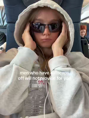 The cover image shows a young woman in a hoodie and sunglasses, looking at the camera with a neutral expression. The background appears to be a public transport setting, with other passengers visible. Text is overlaid on the image.