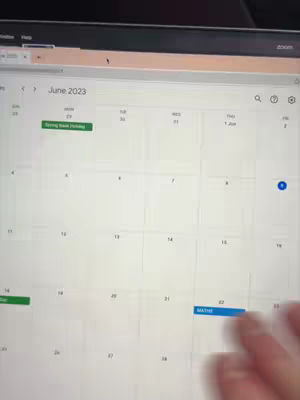 A laptop screen displaying a calendar view for June 2023. The calendar shows dates with highlighted events, including a green-highlighted "Spring Bank Holiday" on the 29th, and a blue-highlighted event on the 22nd, labeled "MATHS". A hand is partially visible, interacting with the screen.