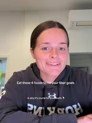 A woman in a black hoodie is centered in the frame, looking directly at the camera and smiling slightly. Text appears on the lower third, with sentences in white font. The background shows a simple room with a white ceiling and a partially visible door on the left. An air conditioning unit is visible at the top right.