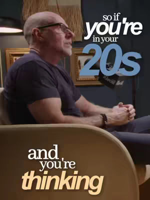 The cover image features a medium shot of a man in his 60s, balding with eyeglasses, seated in an armchair in front of a dark blue wall, where framed pictures hang, and a decorative element in the background. He is turned to the left with hands folded in his lap, and wearing a dark-colored t-shirt. The text overlay includes the phrase 'so if you're in your 20s' in large bold text, and 'and you're thinking' in smaller letters at the bottom left in a contrasting color. The overall composition appears to be for an interview or podcast setting.