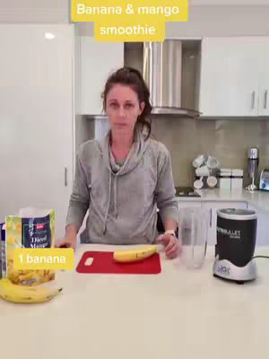 A woman stands in a kitchen, preparing a banana and mango smoothie. Text overlays indicate the smoothie's name, the fruit, and ingredient. The background includes kitchen cabinets and appliances.